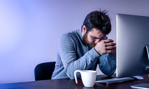 tired man sits front computer with cup coffee colored lighting 2